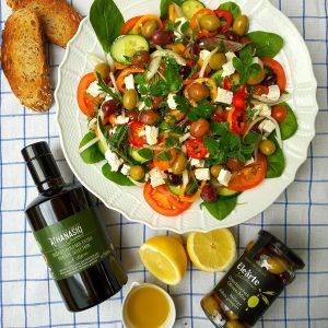 Griechischer Bauernsalat mit frischem Gemüse, Feta, Elearte by Athanasio Griechischer Oliven Mix und Nativem Olivenöl extra auf Servierplatte.